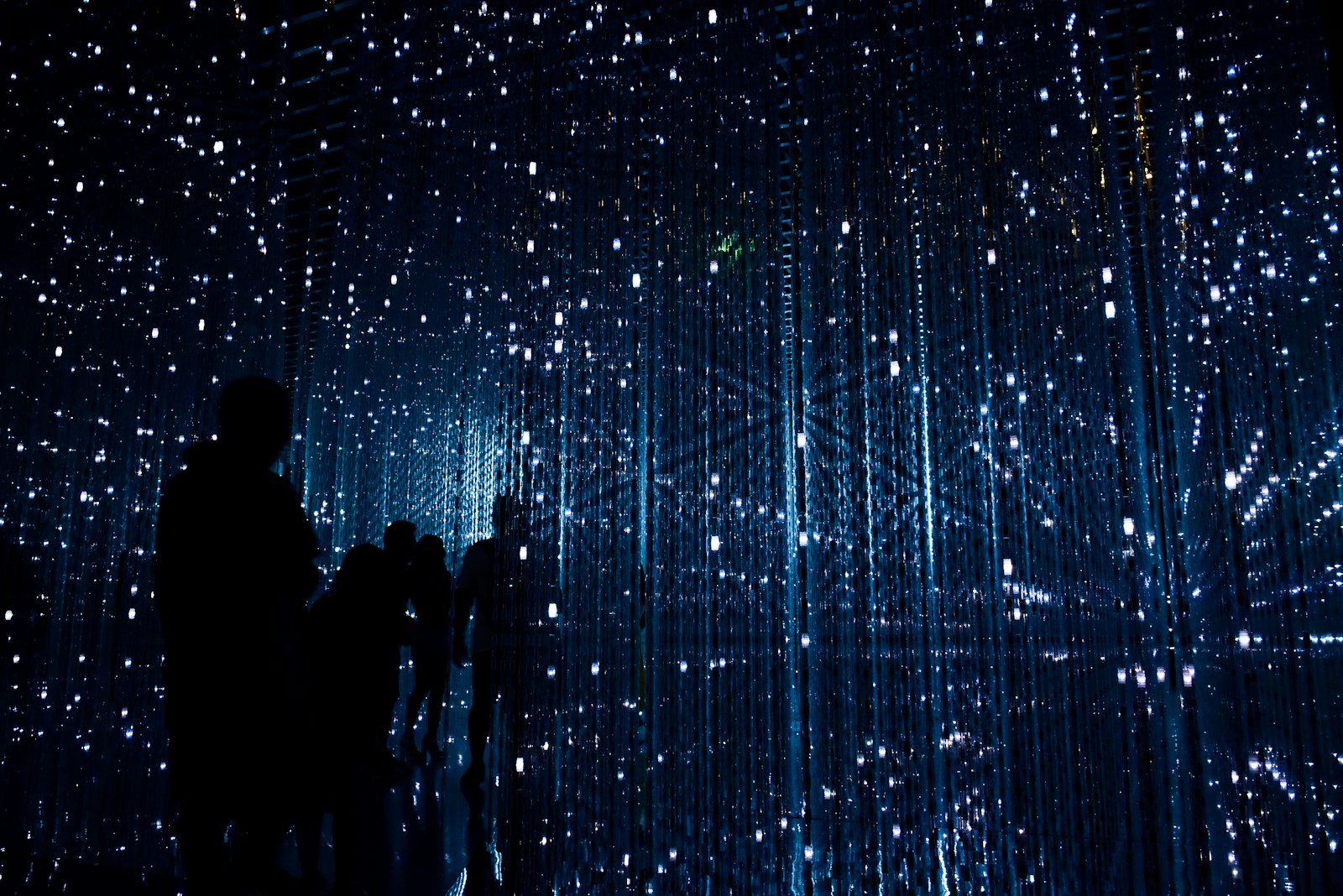 Silhouetted figures walking through an installation of illuminated vertical light strands, evoking continuous data pipelines.
