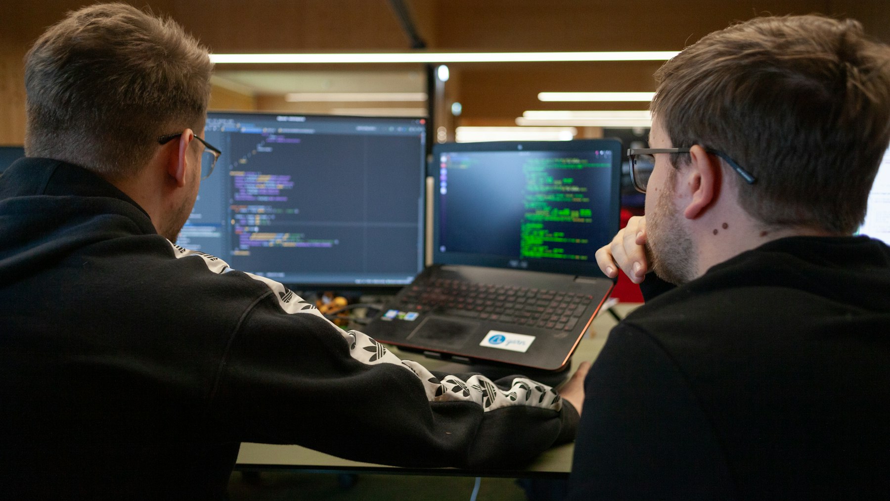 Two engineers looking at code together on a laptop and monitor.